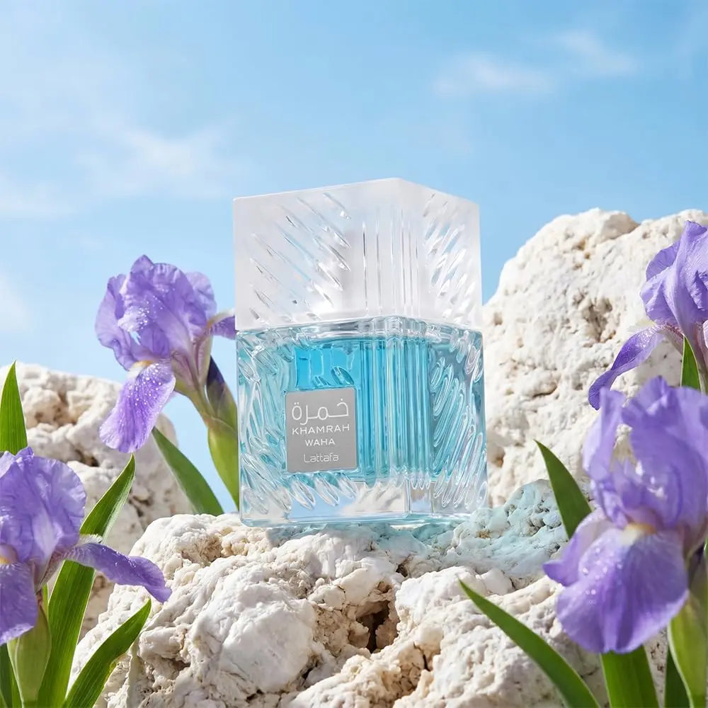Blue perfume bottle with decorative design on a rocky surface with purple flowers