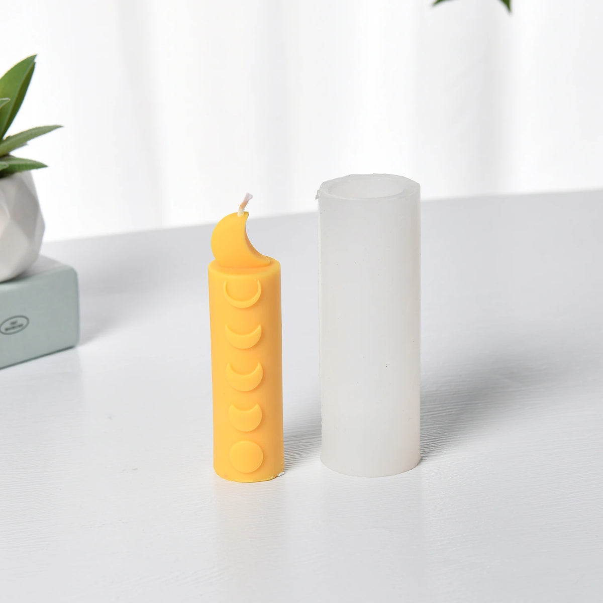 Yellow crescent-top moon-phase pillar example candle beside a white cylindrical silicone mold