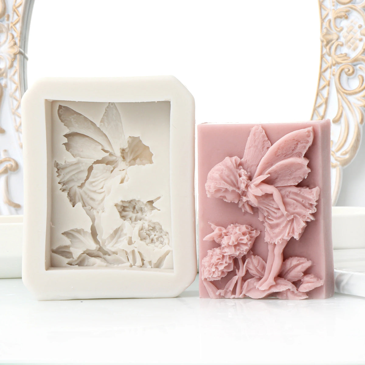 Rectangular pink standing fairy and flower relief casting example beside its white silicone mold