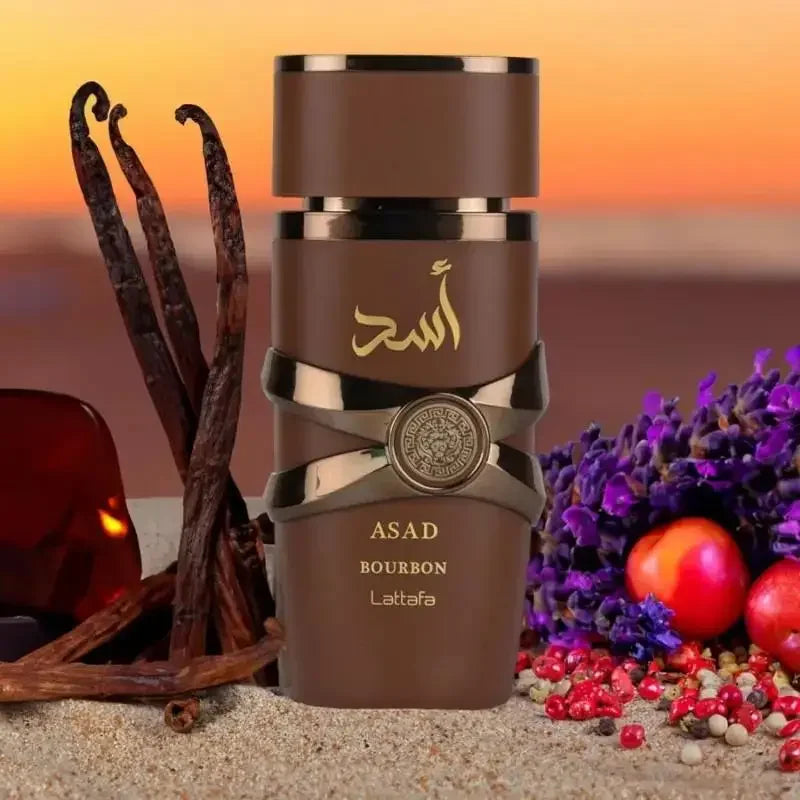 A bottle of ASAD Bourbon Lattafa perfume is displayed on a sandy surface with a sunset background, styled with vanilla beans, purple flowers, red fruits, and spices.