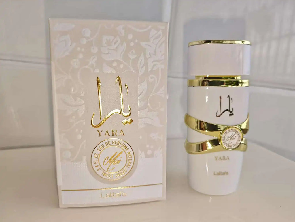 A white Lattafa Perfume perfume bottle with gold bands and Arabic lettering next to its matching white and gold outer box, labeled YARA and Laifan.