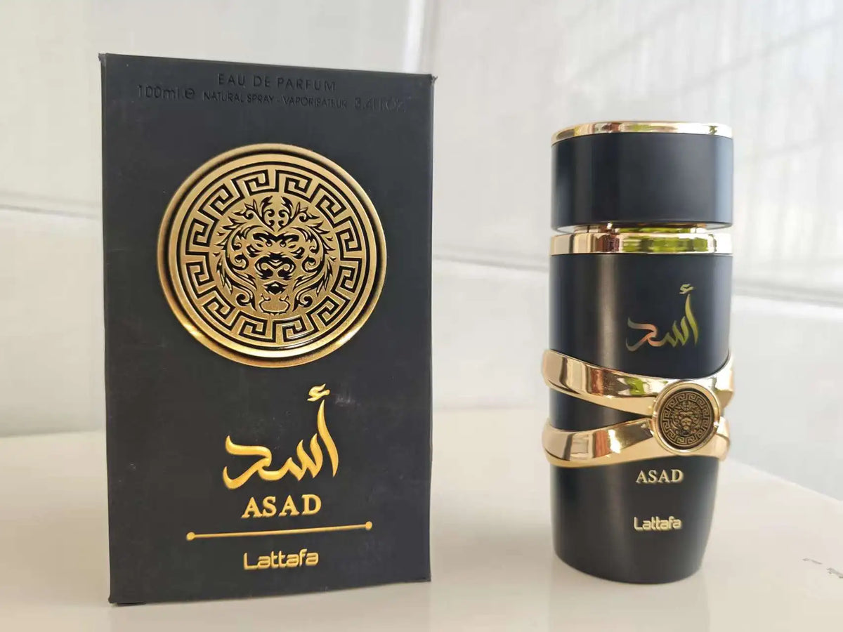 A bottle of ASAD Lattafa fragrance next to its black packaging box with gold detailing, set against a light background.