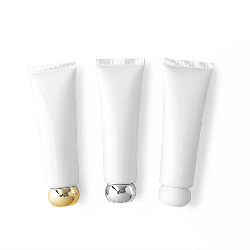 Three white squeeze tubes with gold-tone, silver-tone and white caps