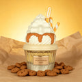 A decorative Lattafa Perfume whipped cream and cookie cup treat styled like a dessert cup, with white whipped cream, caramel drizzle, two striped orange-and-white straws, and scattered chocolate chip cookies on brown paper against a warm yellow background. A small label reads 'Lattafa' and the top pick shows 'Lattafa' again.