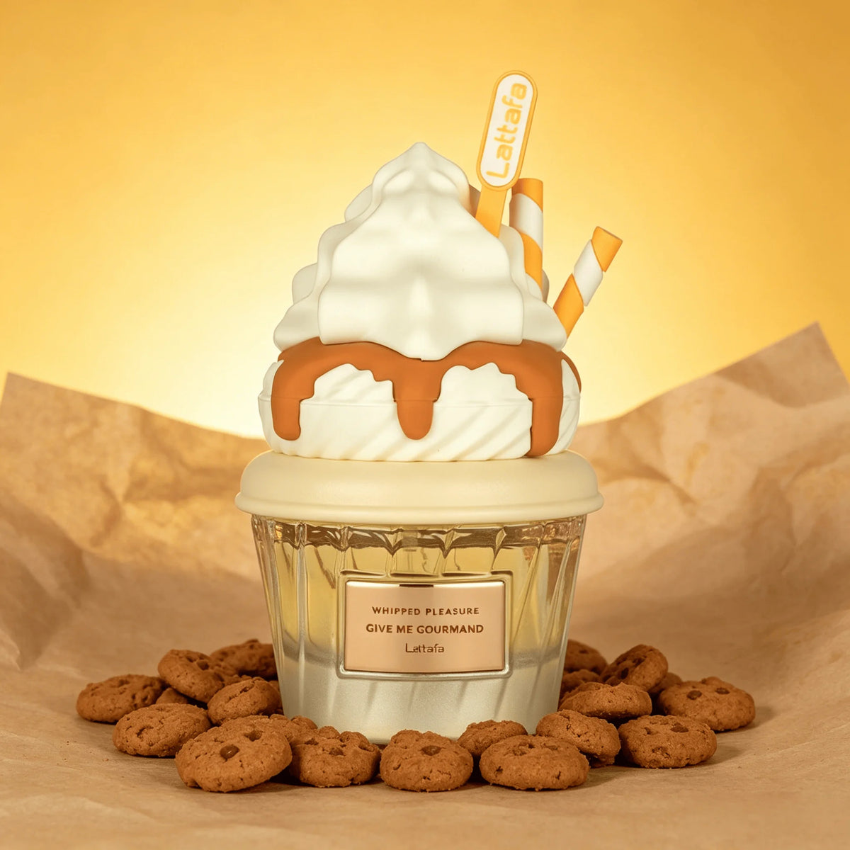 A decorative Lattafa Perfume whipped cream and cookie cup treat styled like a dessert cup, with white whipped cream, caramel drizzle, two striped orange-and-white straws, and scattered chocolate chip cookies on brown paper against a warm yellow background. A small label reads 'Lattafa' and the top pick shows 'Lattafa' again.