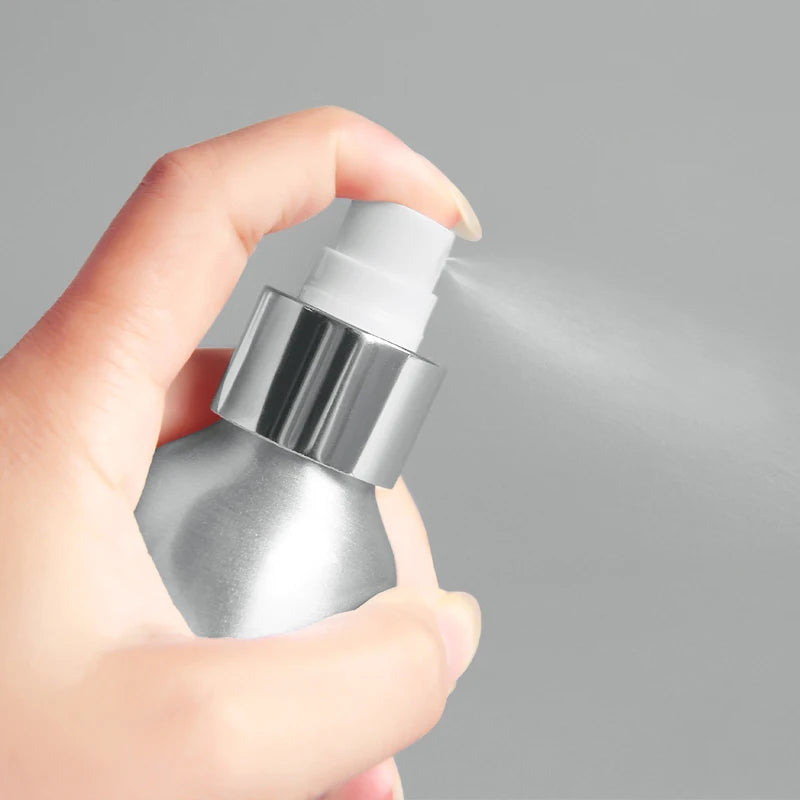 Hand pressing a white spray nozzle on a silver aluminum bottle