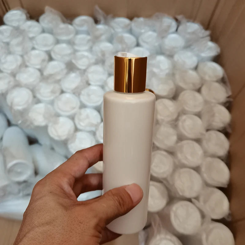 White bottle with gold-tone disc-top cap held above a box of bottles