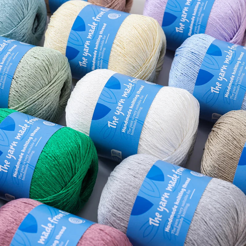 Assorted solid-color linen lace yarn skeins with blue labels, including cream, white, green, blue, pink and gray.