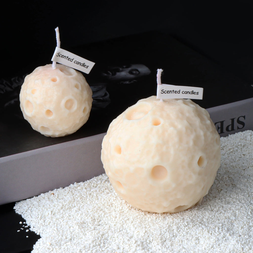 Two ivory moon sphere candles with crater texture, wicks and paper scent tags