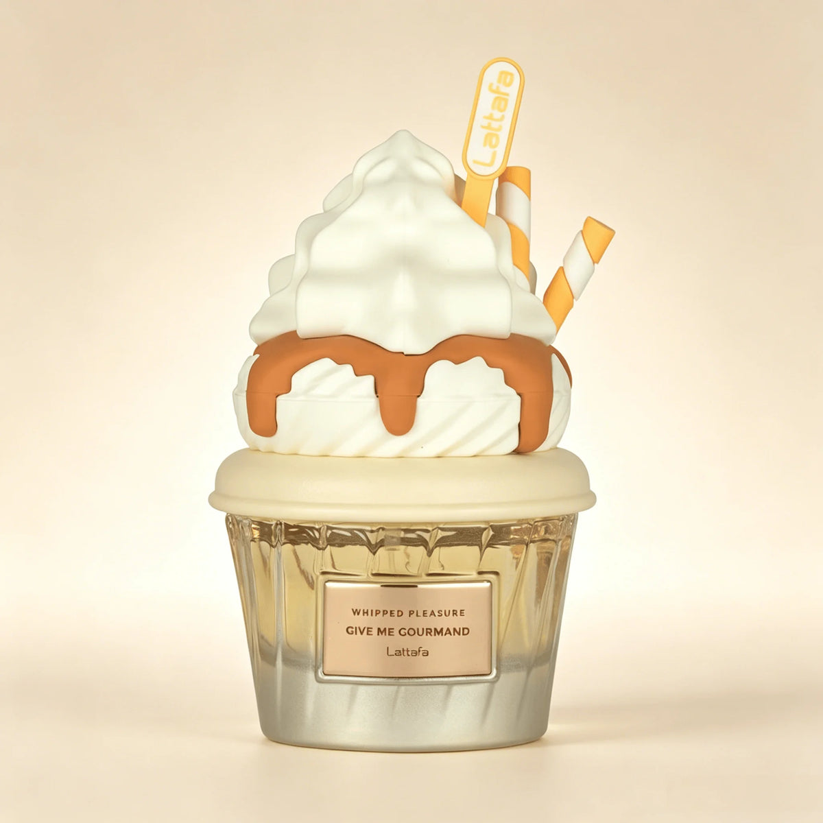 A Lattafa Perfume whipped cream and caramel sauce cupcake-shaped fragrance diffuser or candle. The design features white whipped cream, caramel brown drizzle, a clear ribbed glass cup, and two yellow-and-white striped straws, all set against a warm beige background.