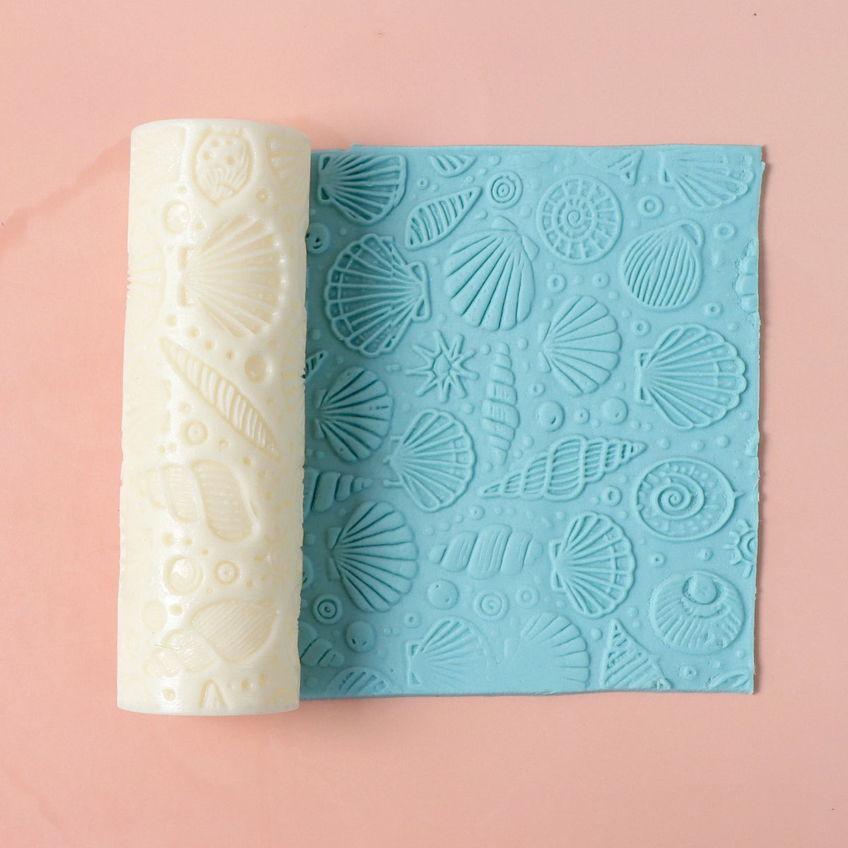 Overhead view of a seashell texture roller and blue patterned panel on a pink background