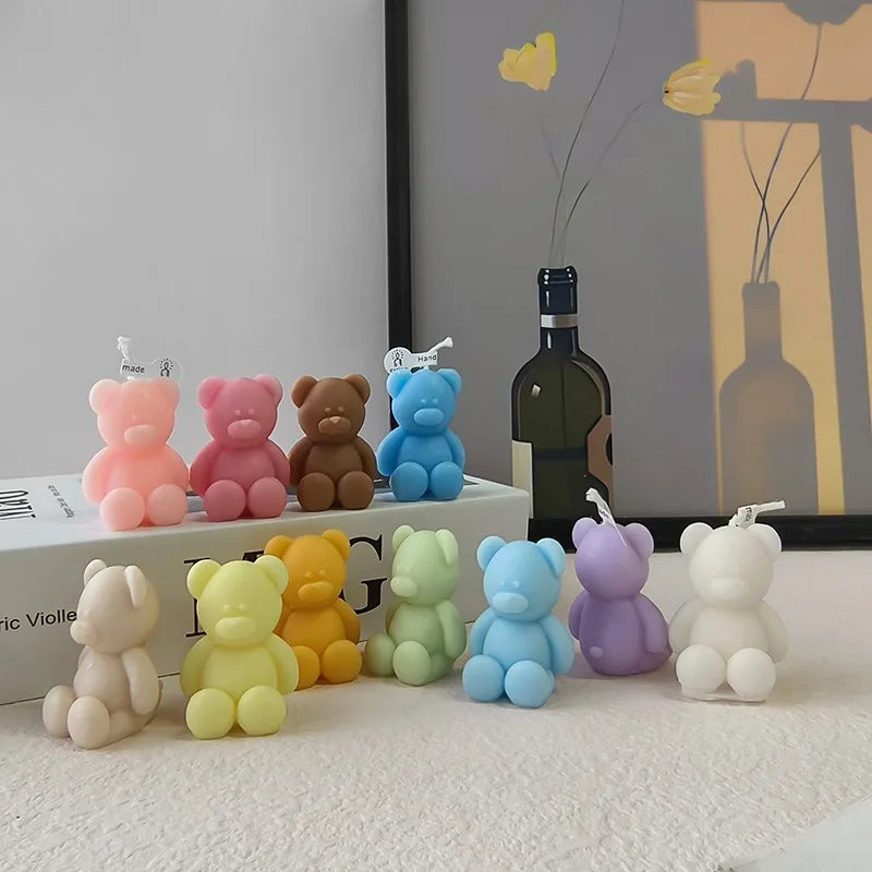Mini teddy bear candles in assorted colors displayed beside books and a dark bottle