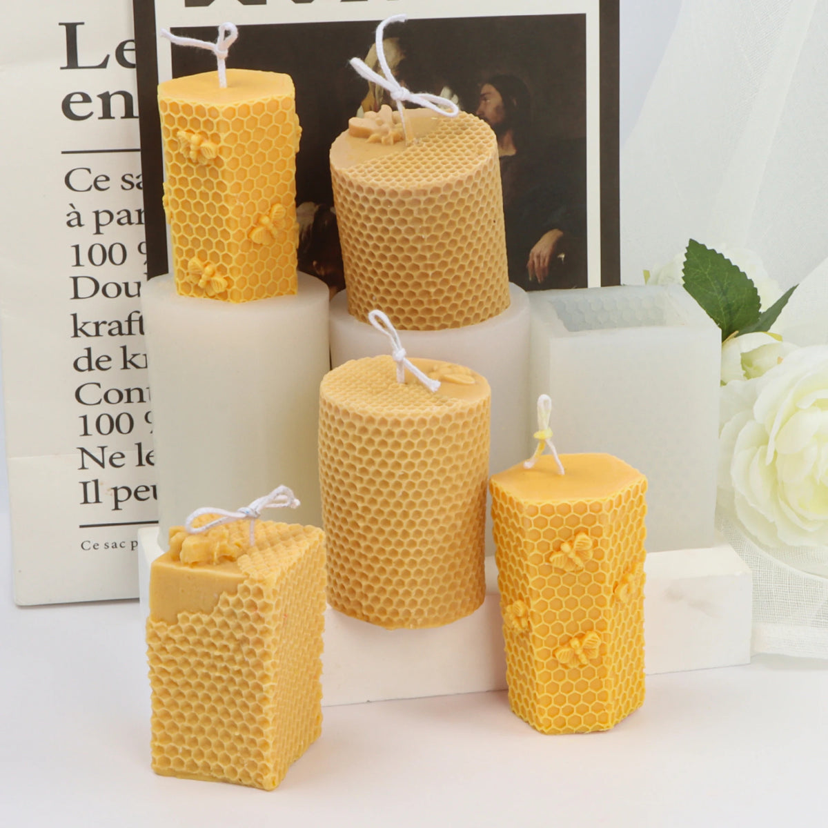 Five bee and honeycomb pillar example candles arranged on white stepped display stands