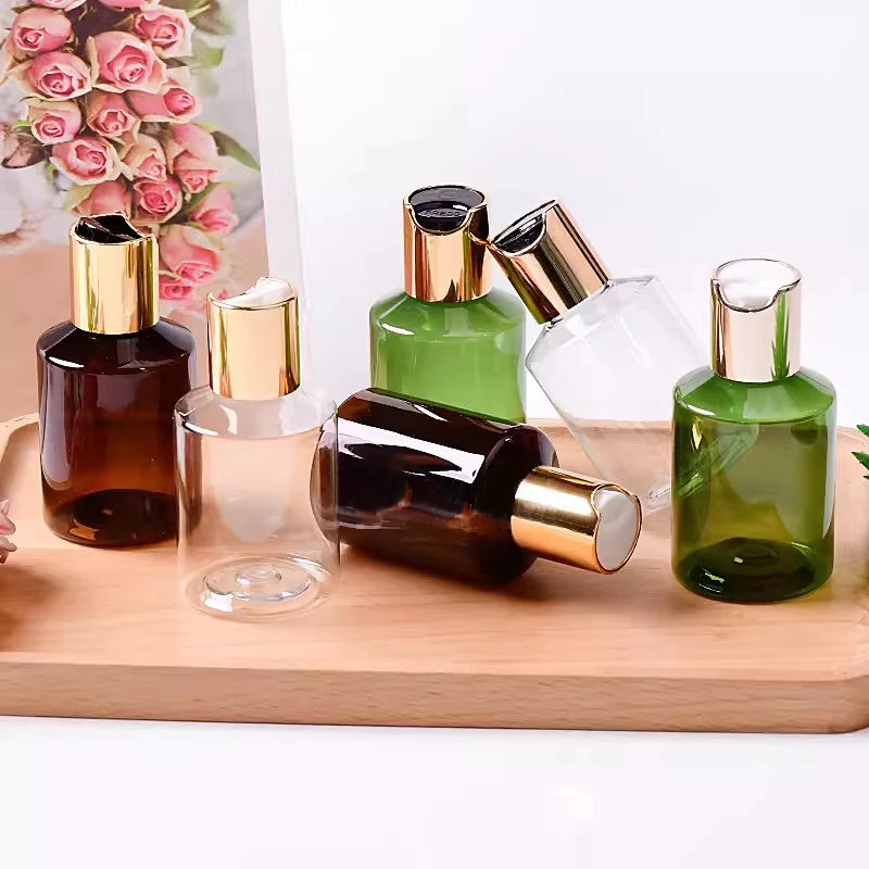 Brown, green and clear cosmetic bottles with gold-tone disc-top caps on a wooden tray