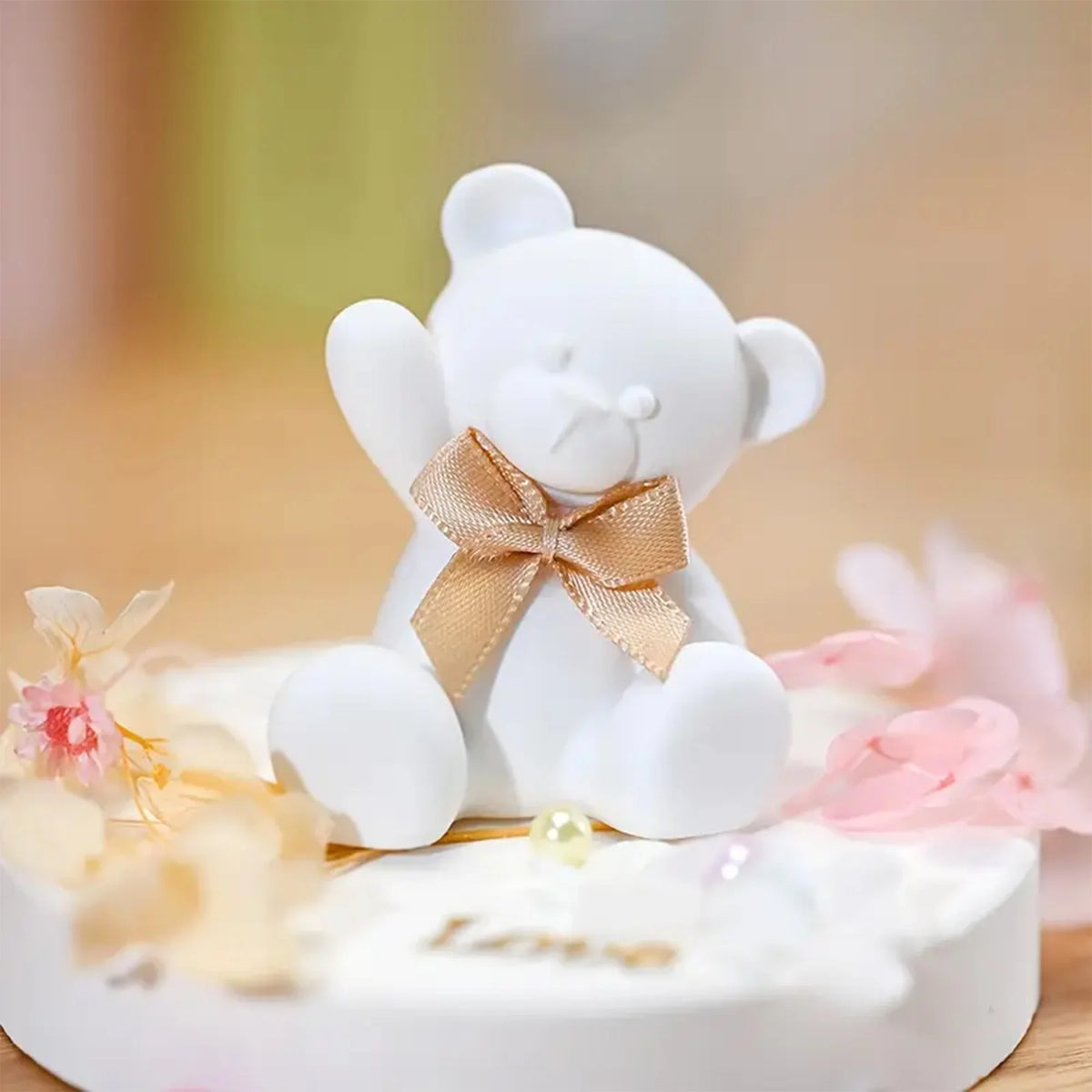 White teddy bear with a gold bow on a white base with flowers