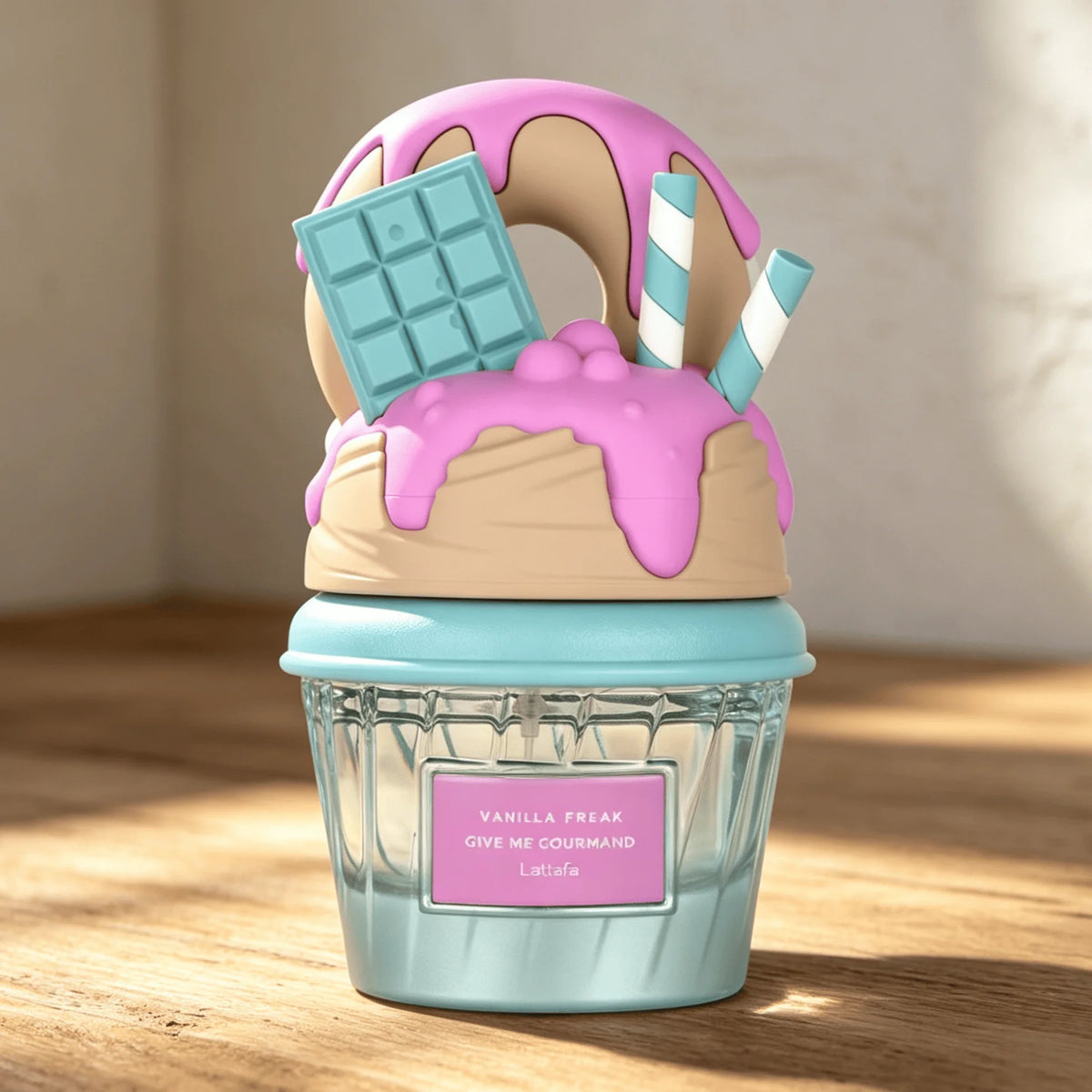 A novelty cupcake-shaped Lattafa perfume bottle with a light blue wrapper, pink frosting, a tan vanilla cream layer, a blue chocolate bar, and striped straws, sitting on a wooden table.