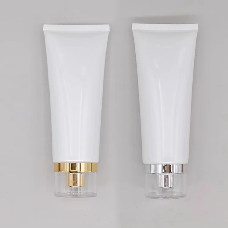 White squeeze tubes with gold-tone and silver-tone dispensing closures under clear covers
