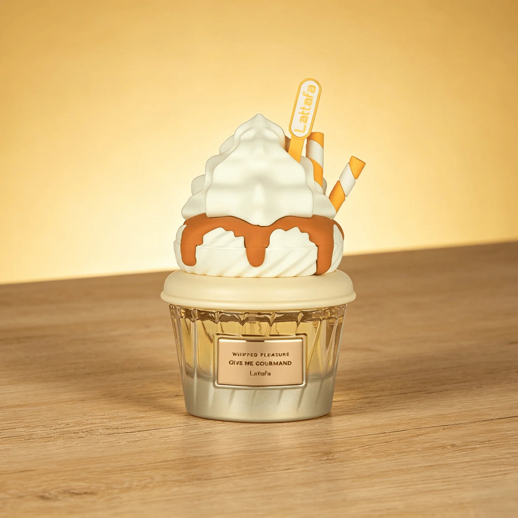 A novelty Lattafa Perfume candle shaped like a whipped cream cupcake with caramel drizzle, sitting on a wooden surface against a warm yellow background. The candle features a textured white whipped cream top with a small 'Le Mignon' sign and striped paper straws, in a clear ribbed glass base with a cream-colored lid and a label that reads 'Whipped Whiskers Give Me Gourmand LEMON'.