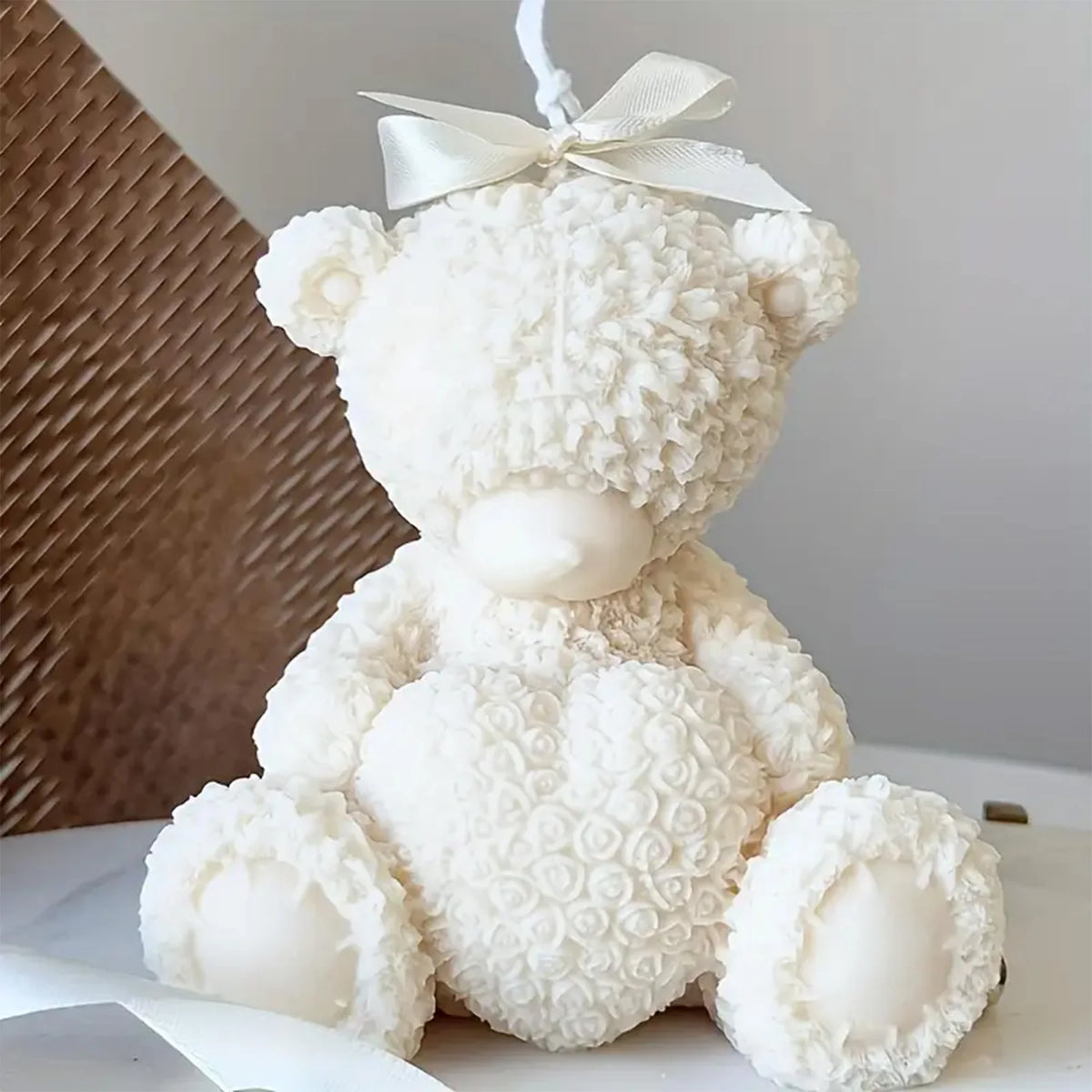 Close-up of ivory seated teddy bear example candle with rose-textured heart and ribbon above its head