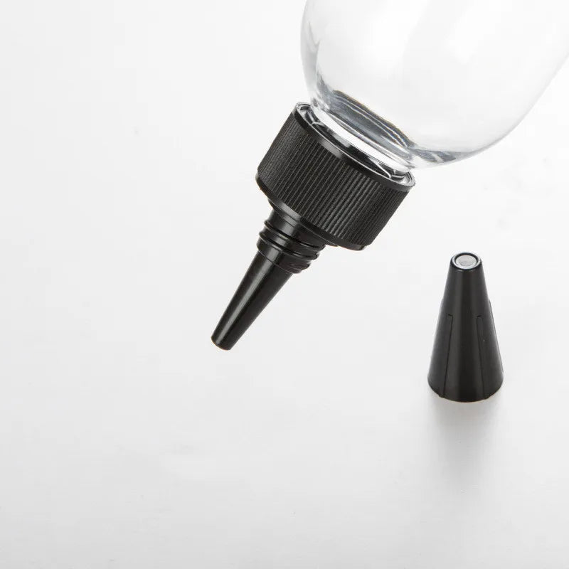 Clear bottle with black pointed nozzle and detached tapered tip cover