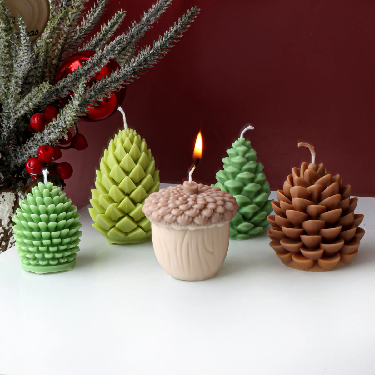 Set of decorative candles shaped like pine cones, acorns, and Christmas trees on a white surface with a red background.