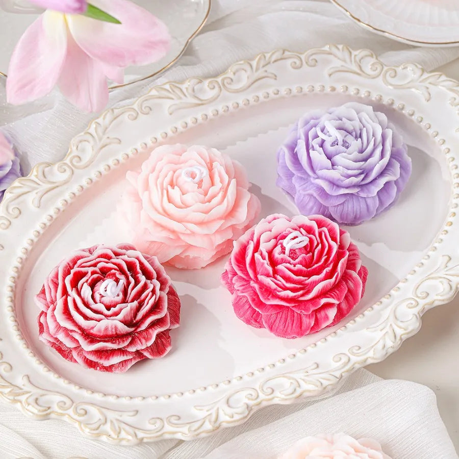 Peony flower candles with layered petals in pink, purple and red on a white tray
