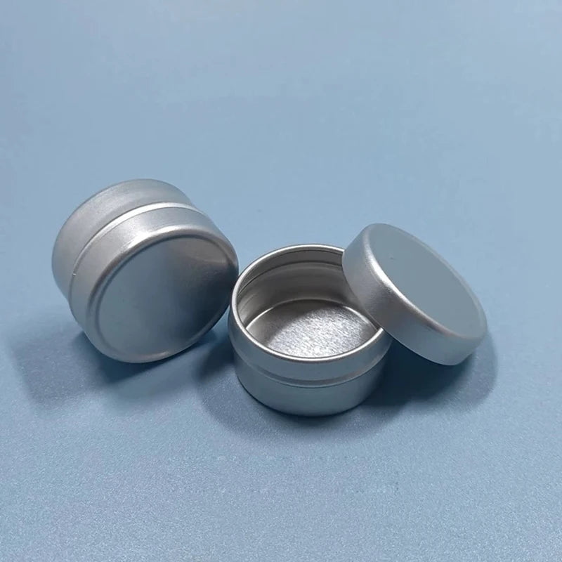 Two round silver aluminum cosmetic tins, one open with its lid beside it