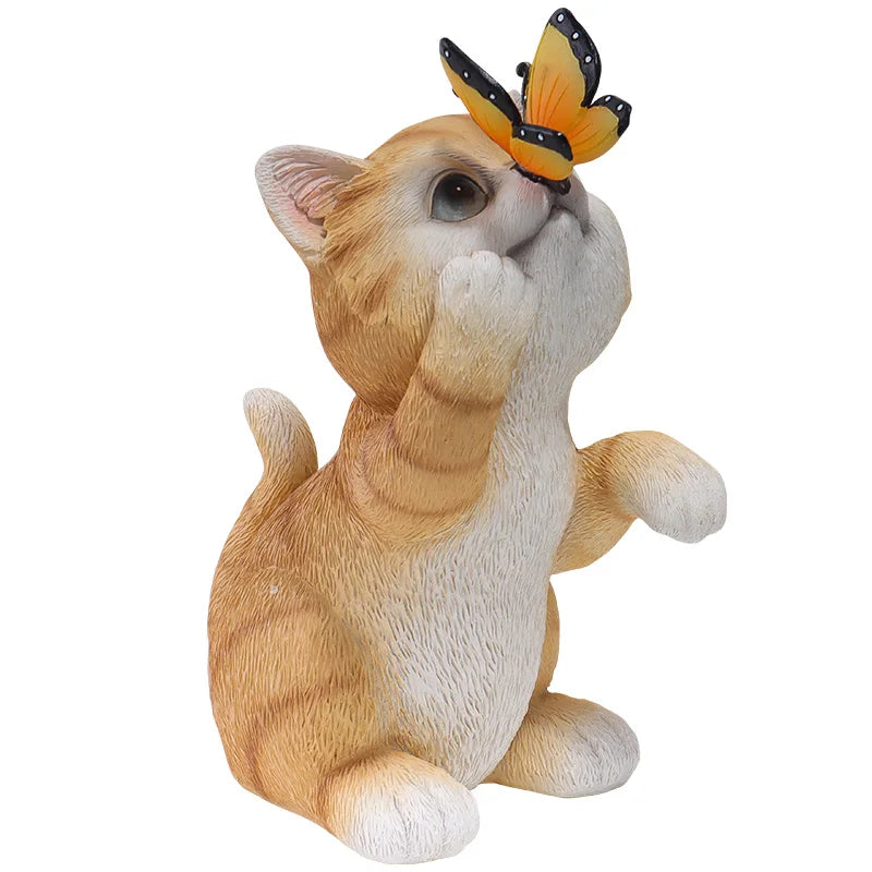 A resin figurine of a cute ginger and white kitten touching its nose with its paw while a yellow and black butterfly rests on its forehead, set against a plain white background.