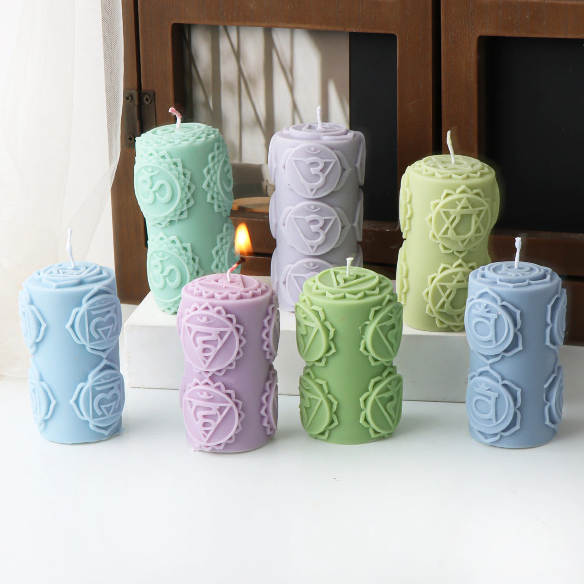 Seven pastel pillar example candles with raised chakra-style symbols, including one lit pink candle
