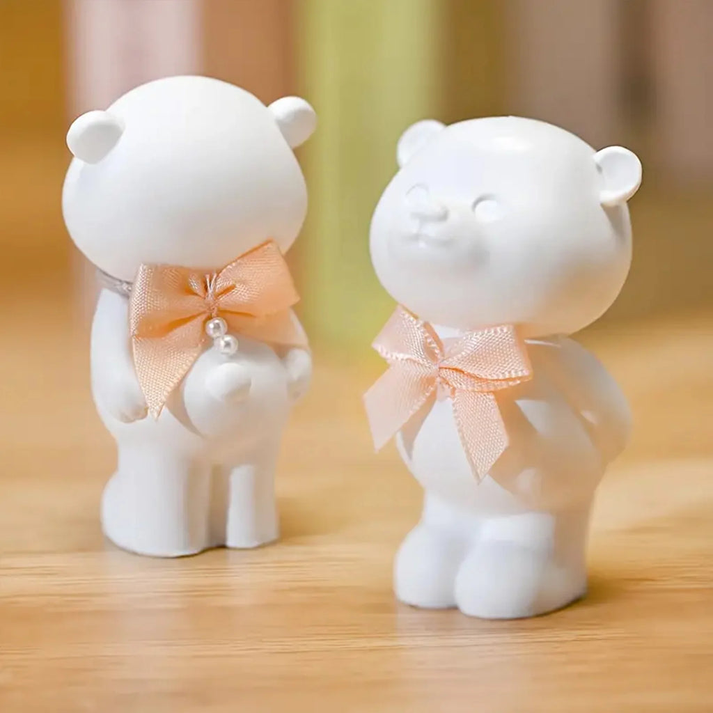 Two white bear figurines with pink bows on a wooden surface