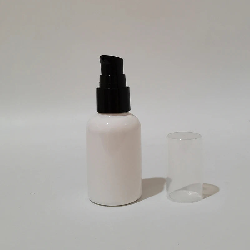 White empty round bottle with a black pump and clear protective cover beside it