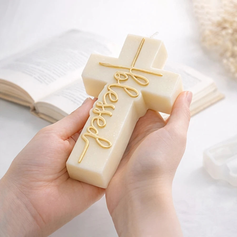 Hands holding an ivory cross example candle with gold-colored Blessed lettering