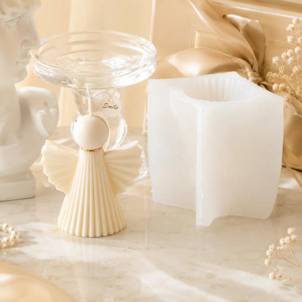 Ivory pleated angel example candle with fan-shaped wings beside a white silicone mold