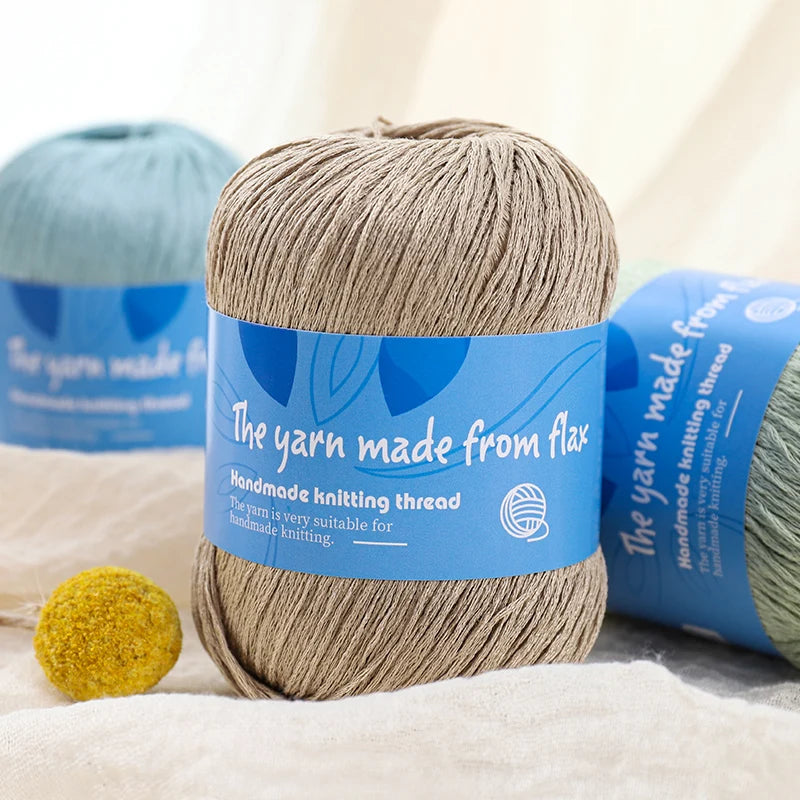 Beige linen lace yarn skein with a blue flax label, displayed beside pale blue and pale green yarn.