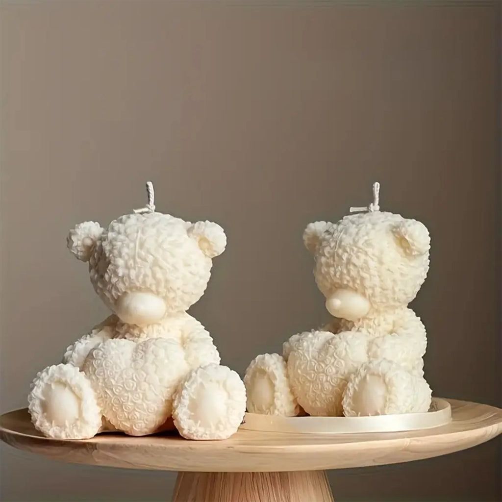 Two ivory seated teddy bear example candles holding textured hearts on a round wooden stand