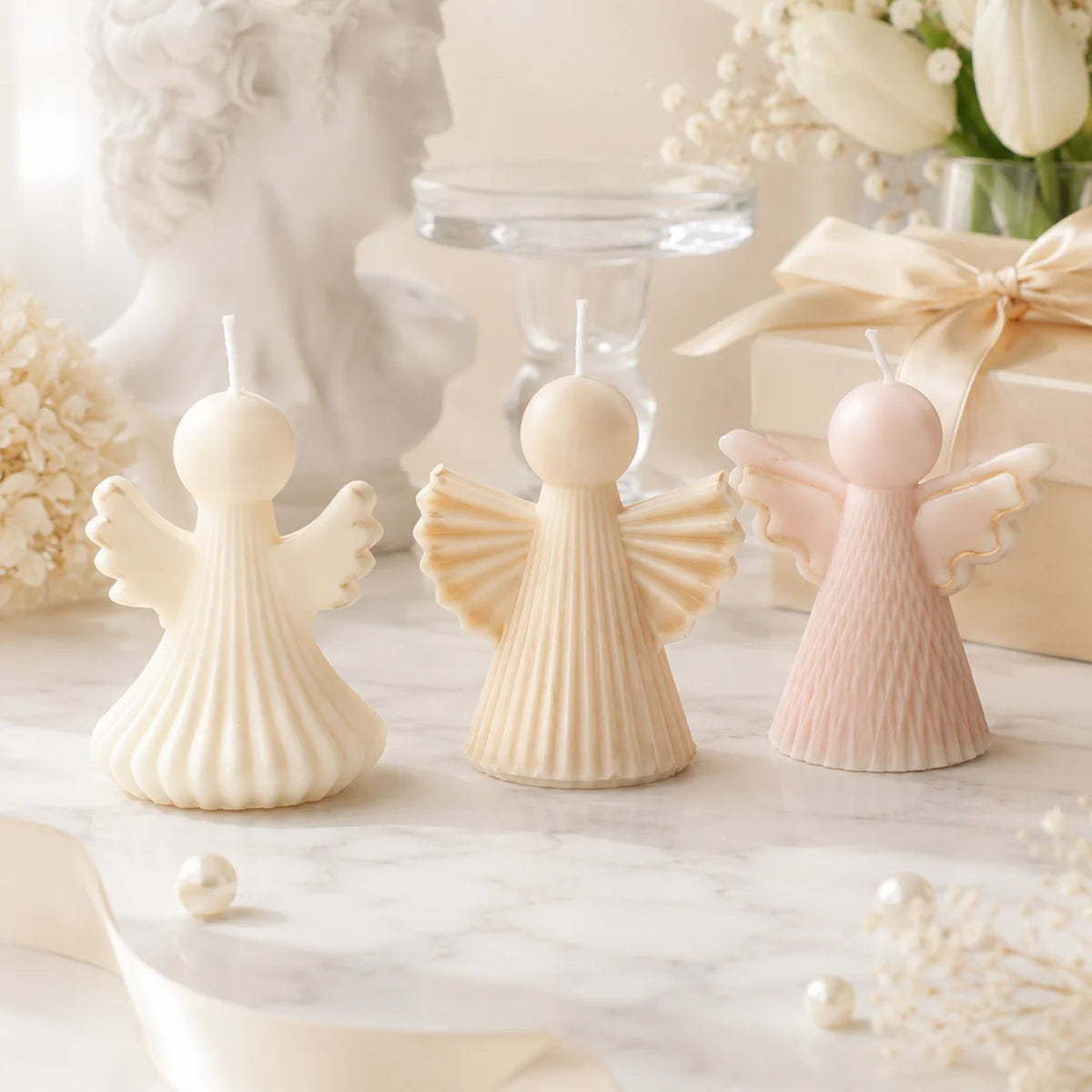 Three ivory and pale pink angel example candles with pleated or textured robes and spread wings