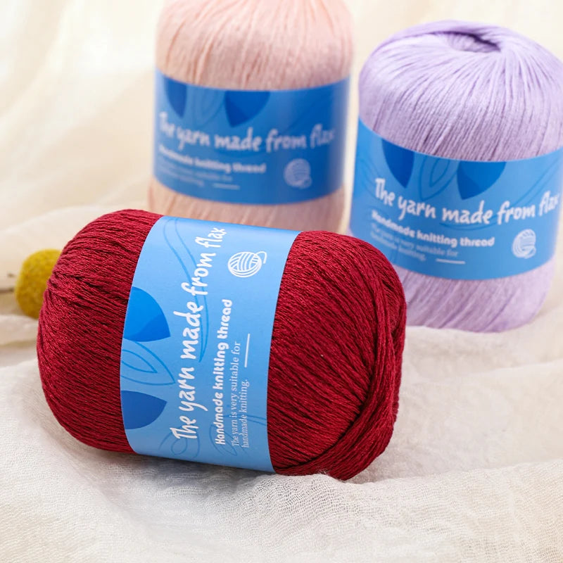 Deep red linen lace yarn skein with a blue label, with blush pink and lavender skeins behind it.