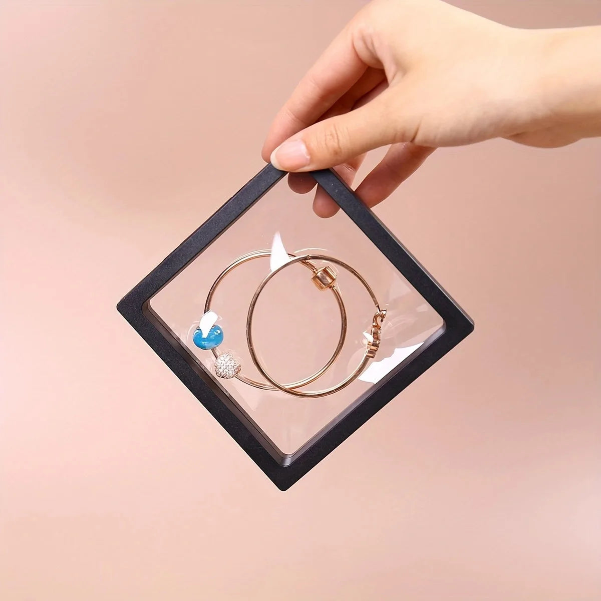Hand holding a clear jewelry display box with gold hoop earrings on a pink background