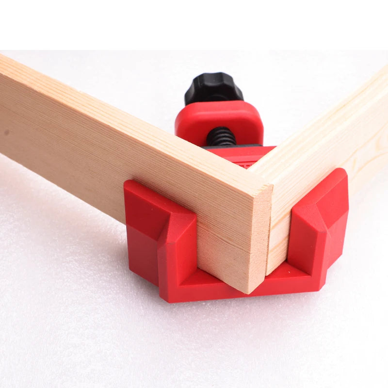 Red corner clamps securing two light-colored wooden boards at a 90-degree angle, with a red and black adjustment screw visible.