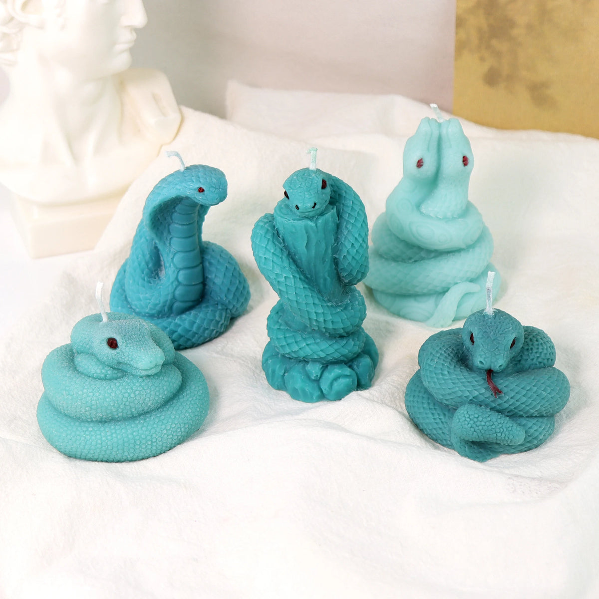 Five turquoise snake example candles with coiled, raised-head and hooded cobra designs