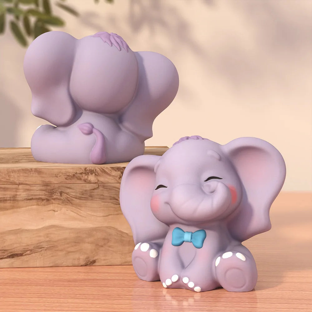 Two lavender elephant figurines on a wooden surface, one facing away and one facing forward with closed eyes, pink cheeks, a blue bow tie, and small white dot accents on its feet and ears.
