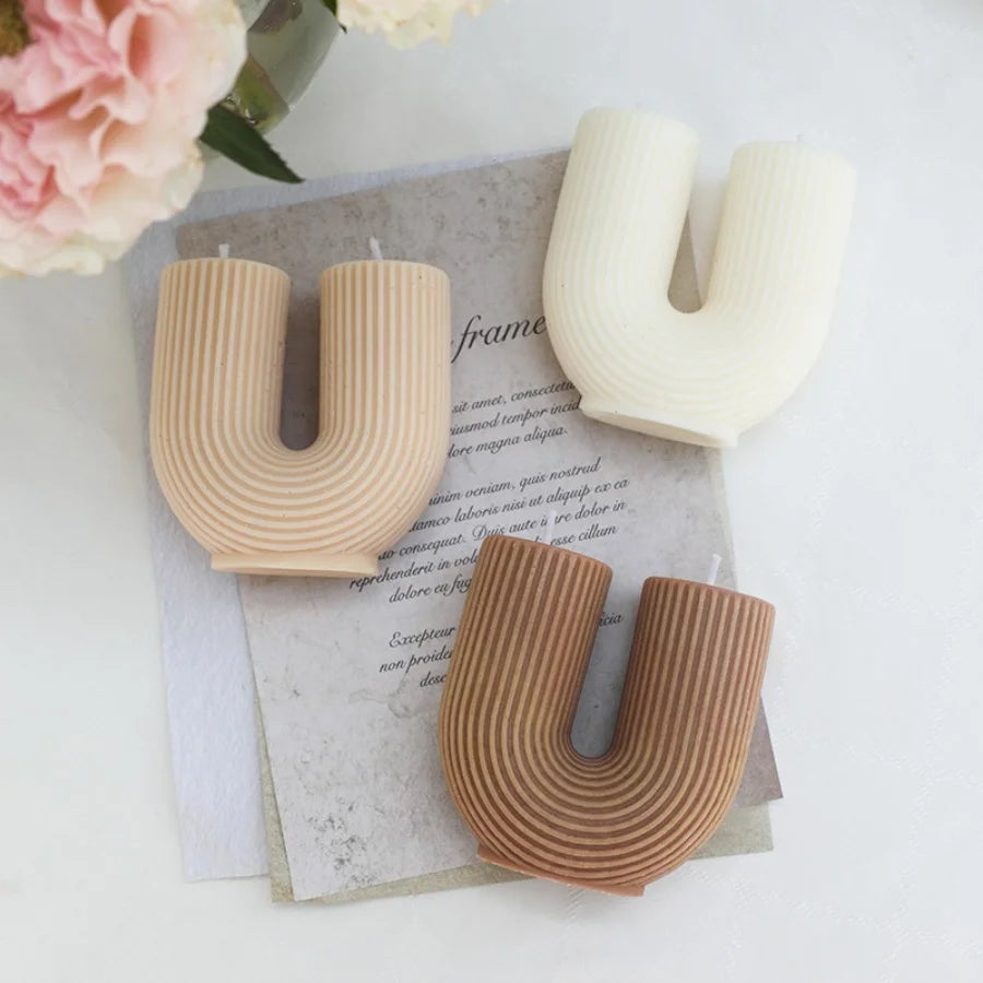 Three letter 'U' shaped candles on a surface with flowers in the background