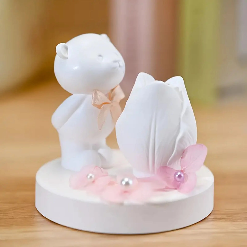 Decorative figurine of a white bear holding a white flower with pink petals on a wooden surface.