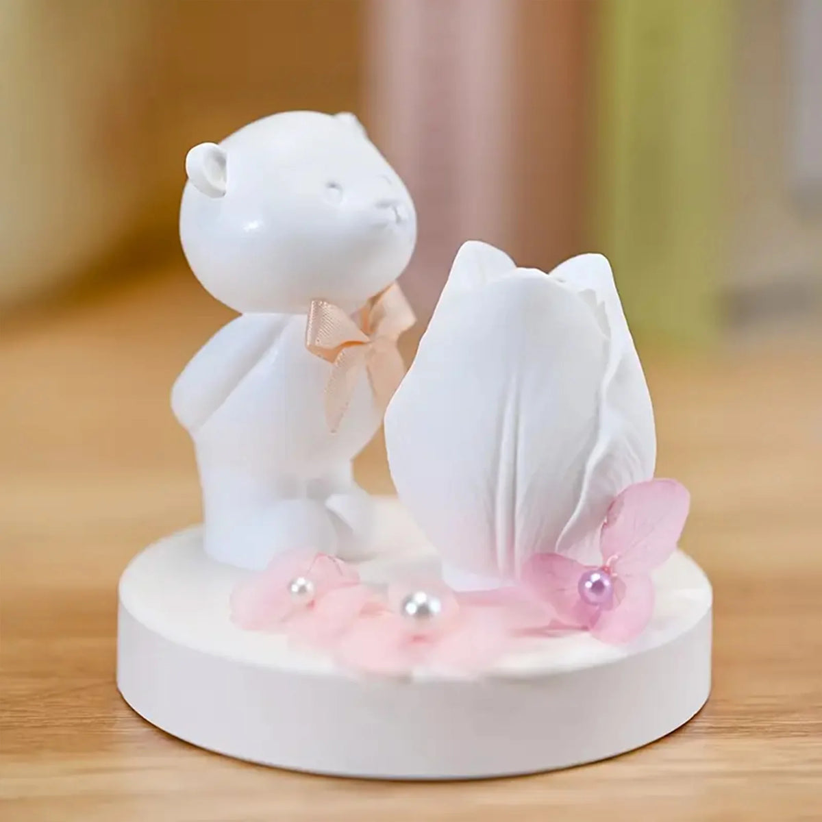 Decorative figurine of a white bear holding a white flower with pink petals on a wooden surface.