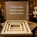 Open cardboard box containing four light wood picture frames in different sizes, with white text on the inside lid reading '15x15cm x3pcs', '20x20cm x3pcs', and '30x30cm x3pcs'. The box is placed on a wooden table in a room with paintings and a bust in the background.