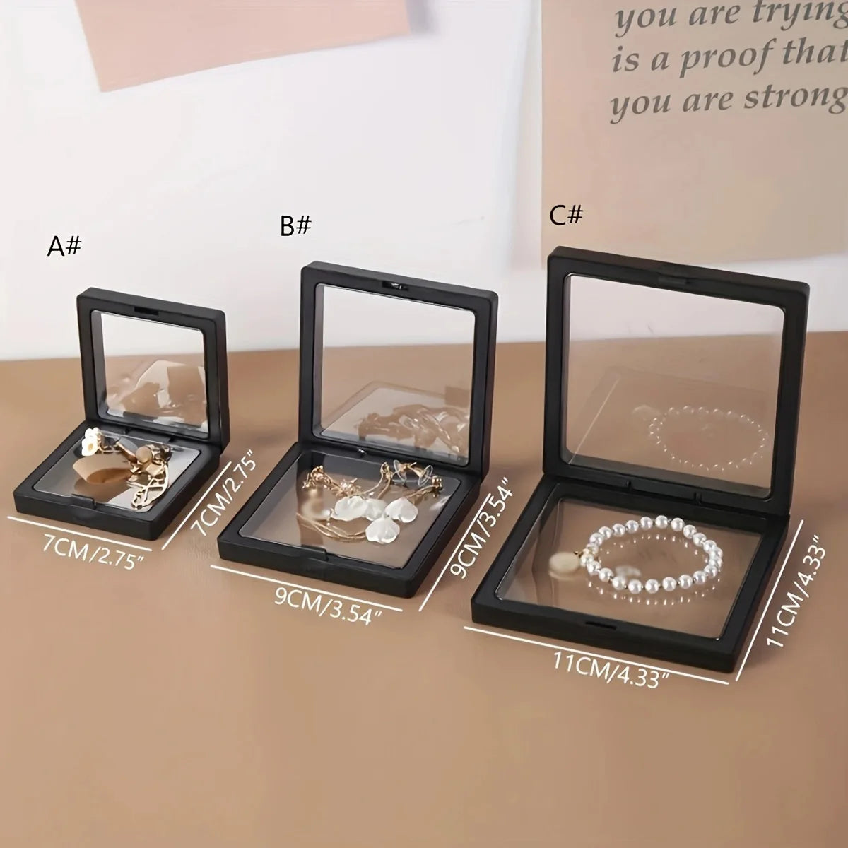 Three black jewelry display cases with jewelry items and measurements on a beige surface.