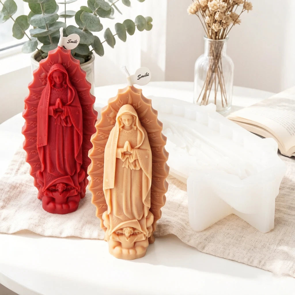 Red and tan Virgin Mary example castings beside greenery, a book and a white silicone mold