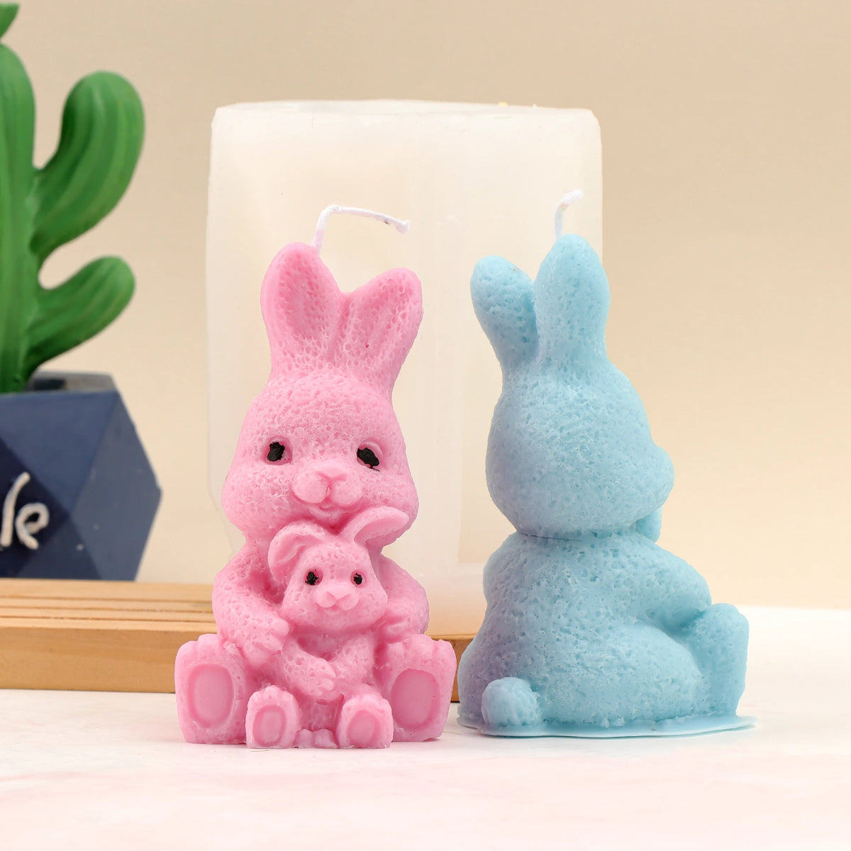 Front of a pink parent-and-baby rabbit candle and rear of a blue example beside a white mold