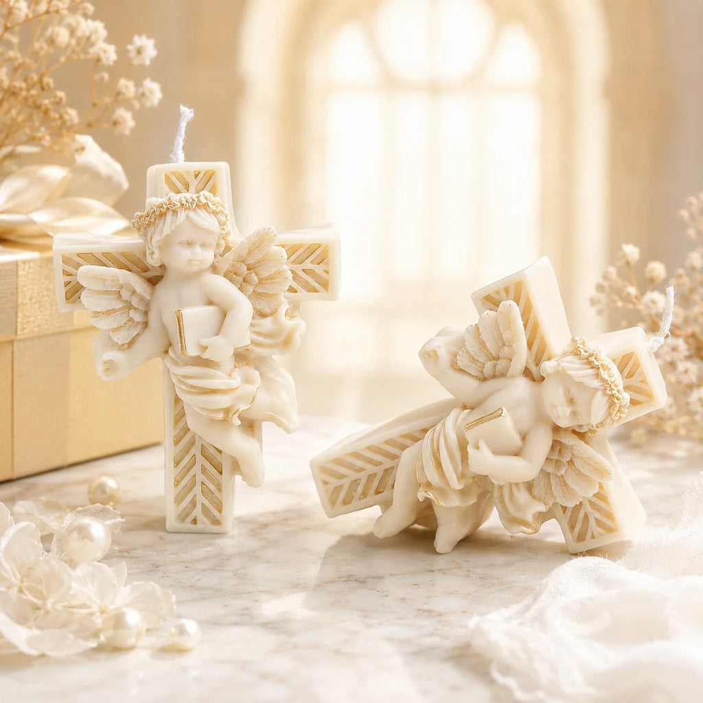 Two ivory and gold-colored cross example candles with a winged cherub holding a book