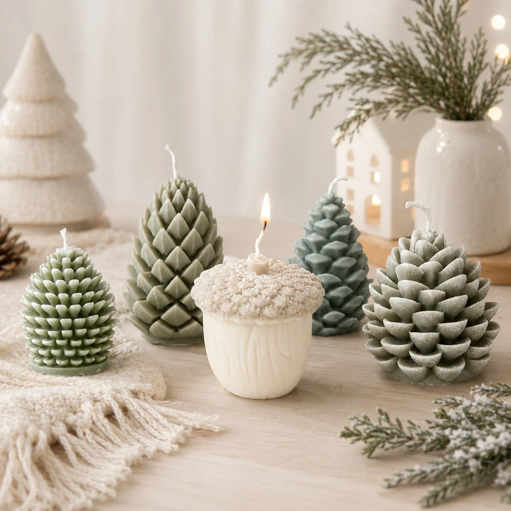 Green pinecone and ivory acorn example candles arranged with winter greenery, with the acorn candle lit